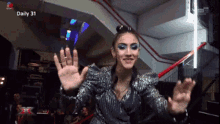 a woman in a silver sequined dress is waving her hands in front of a daily 31 sign