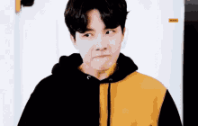a young man is wearing a black and yellow hoodie and making a funny face .