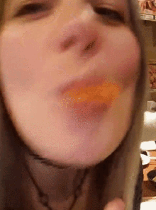 a close up of a woman 's face with a piece of orange in her mouth
