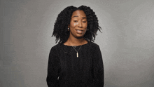 a woman with curly hair is wearing a black shirt and a gold necklace