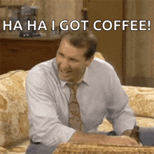a man in a suit and tie is sitting on a couch and laughing with the words " ha ha i got coffee " .