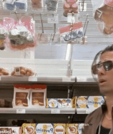 a man wearing sunglasses is standing in front of a shelf with boxes of initiatives on it