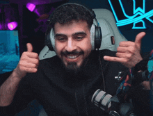 a man wearing headphones and giving a thumbs up while sitting in front of a microphone