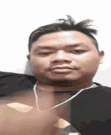 a man wearing a black shirt and a silver chain around his neck is making a funny face .