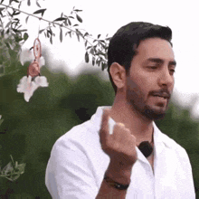 a man with a beard is standing in front of a flower and giving the middle finger .