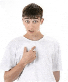 a young man in a white t-shirt is pointing to his chest .
