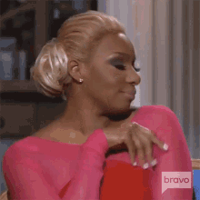 a woman in a pink top is sitting in a chair with her hands on her chest and a bravo logo in the corner .