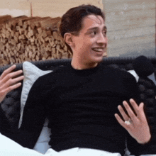a man in a black shirt is sitting on a couch and smiling