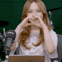a woman making a heart shape with her hands in front of a microphone that says now