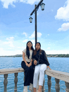 two girls sitting on a railing with one wearing a black sweatshirt with the letter c on it