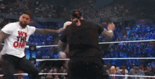 two men are wrestling in a wrestling ring and one of them is wearing a shirt that says we the one
