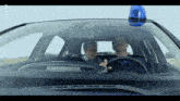 two men are sitting in a car with a blue light on top of the windshield