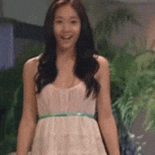 a woman in a white dress is smiling and standing in front of a plant .