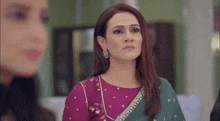 a woman in a purple top and a green saree is standing next to another woman .