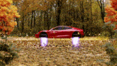 a red car is driving through a forest with leaves flying around it