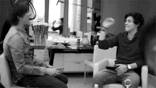 two men are sitting in chairs talking to each other in a room .