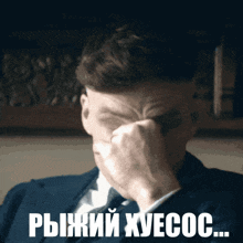 a man in a suit and tie is covering his face with his hand and the words " рыжий хуесос " are below him