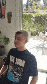 a man wearing a new york t-shirt is sitting in front of a window
