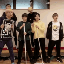 a group of young men are standing next to each other in a room holding mopsticks .