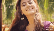a woman wearing a purple top and earrings is smiling .
