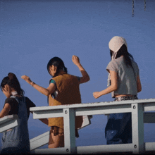 three girls are standing on a fence with one wearing a white hat