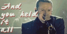 a man singing into a microphone with the words " and you held it all " written on the wall behind him