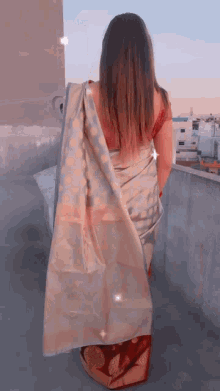 a woman in a saree stands on a balcony