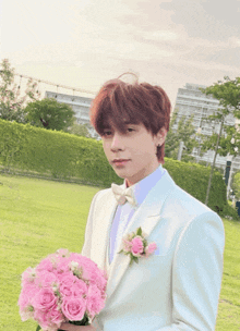 a man in a white suit holding a bouquet of pink roses