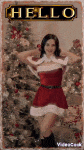 a woman in a santa costume is standing in front of a christmas tree and says hello