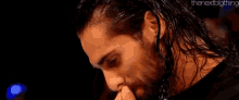 a man with long hair and a beard is eating something with his hands .