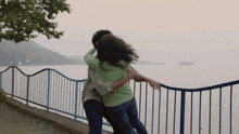 a man is holding a woman in his arms near a fence overlooking a body of water