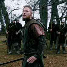 a man with a beard stands in front of a group of soldiers with spears