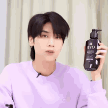 a man wearing a purple sweater holds a bottle of ryo shampoo