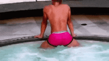 a man is kneeling in a hot tub wearing pink shorts .