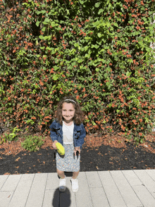 a little girl standing in front of a bush with red berries