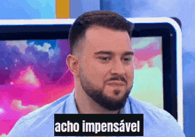 a man with a beard is sitting in front of a television with a sticker that says acho impessavel