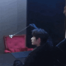 a man in a black jacket is looking up at a red box in a dark room .