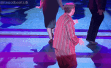 a man in a red shirt is dancing on a stage with purple lights behind him