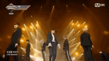 a group of men are dancing on a stage with mnet in the background