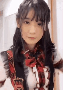 a young girl wearing a plaid shirt and a red bow tie is looking at the camera .