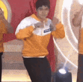 a man in an orange sweatshirt is dancing on a stage with other people .