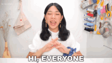 a woman in a white shirt says hi everyone with her hands crossed