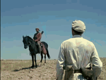 a man standing next to a man riding a horse in a field