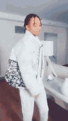 a person wearing a white jacket and white pants is dancing in a room