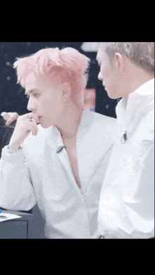 two men with pink hair are standing next to each other and talking .