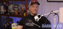 a man in a black shirt is sitting in front of a microphone with dark web written on the bottom