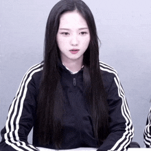 a girl with long black hair is wearing a black jacket with white stripes