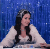 a woman wearing a crown and a white dress is sitting at a table
