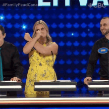 a woman in a yellow dress is standing in front of a microphone on a family feud game show .