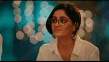 a woman wearing glasses and a white shirt looks at something